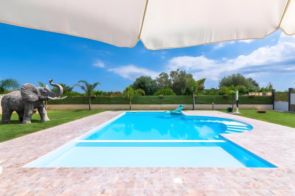 an elephant standing next to a swimming pool with an umbrella at Jungle Holiday Villa in Marina dʼAvola