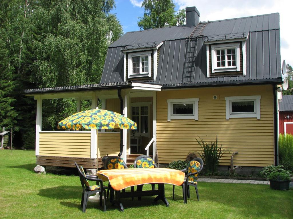 a yellow house with a table and chairs and an umbrella at Stuga på Brattmon in Sysslebäck