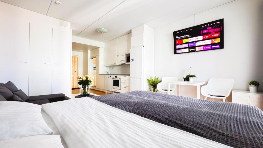 a white bedroom with a large bed and a kitchen at City center brand new studio, parking in Oulu