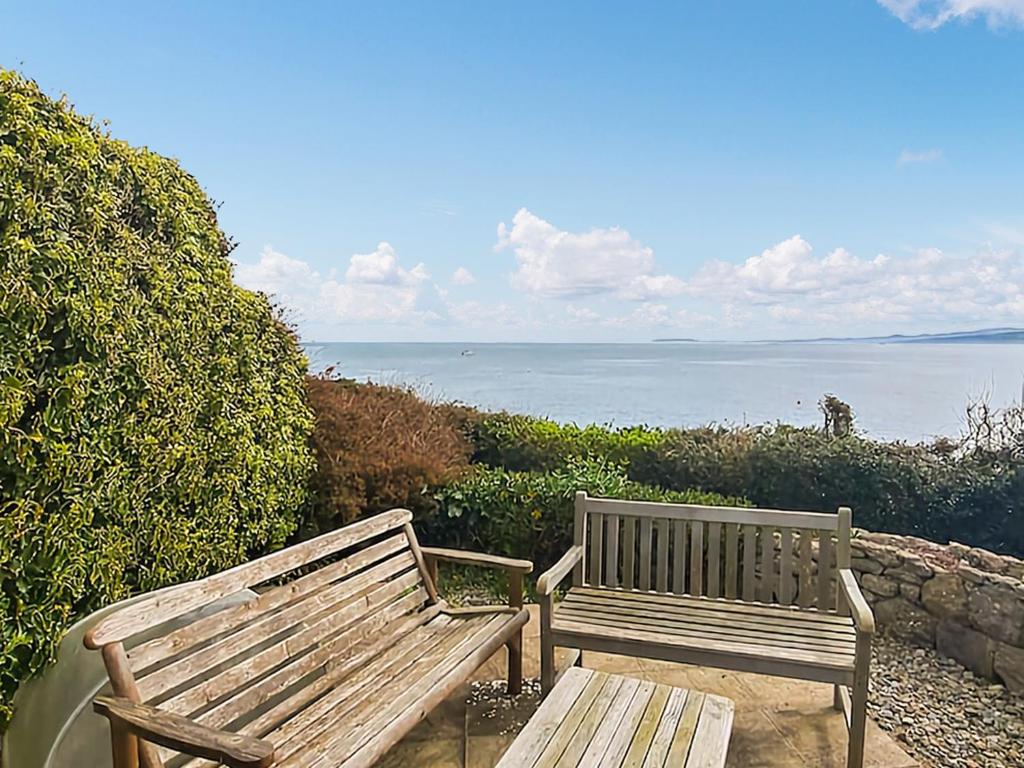 two wooden benches sitting next to the ocean at Gosteg in Moelfre