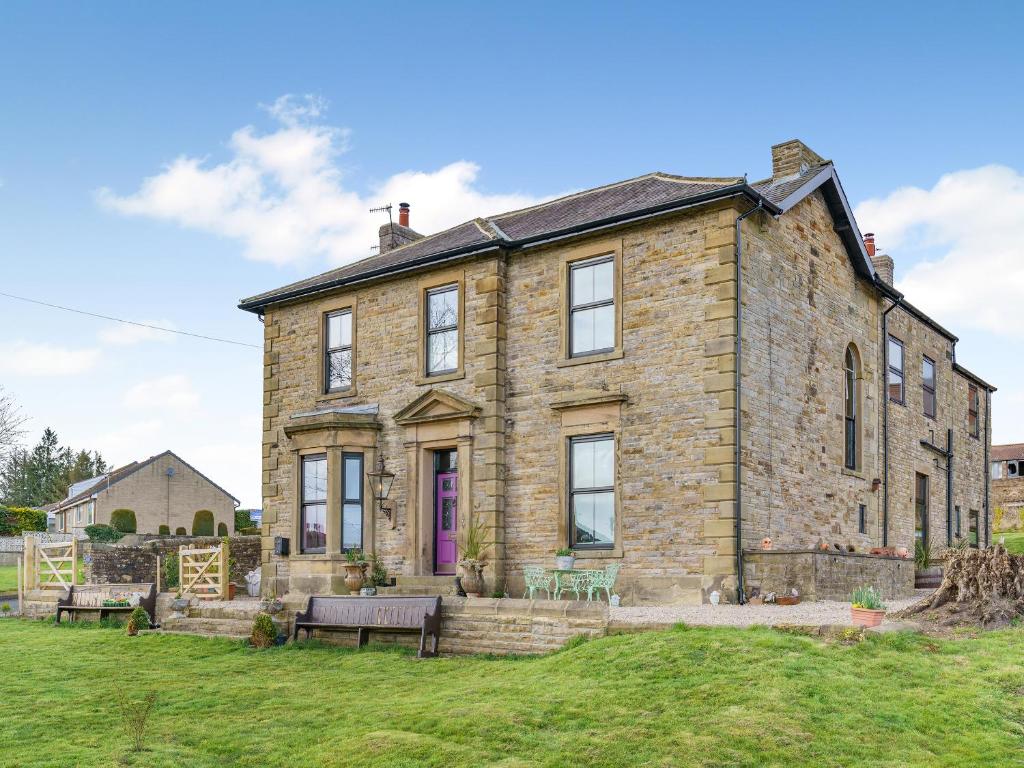 an old stone house with two benches in front of it at Greystonedale Mansion Holiday Retreat in Haltwhistle