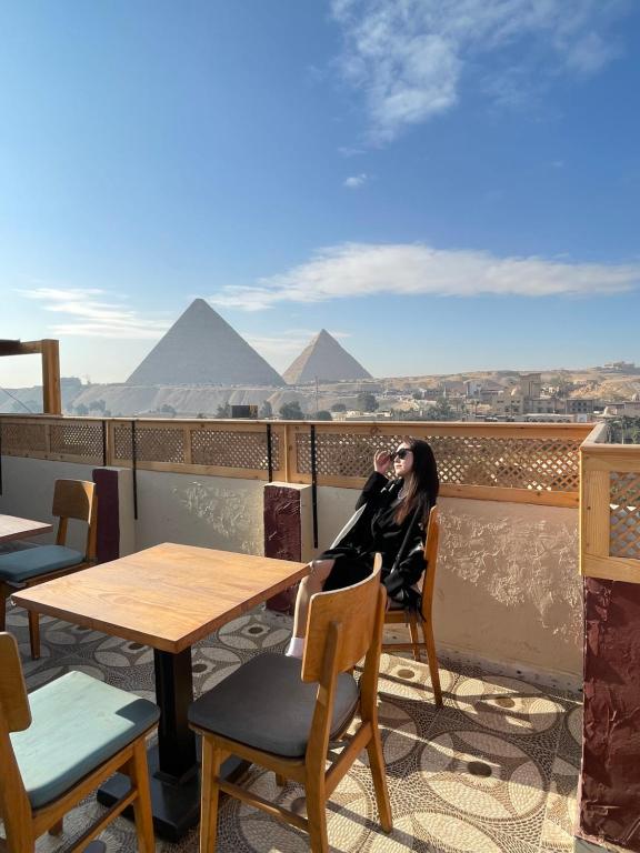 a woman sitting at a table on a balcony with pyramids at Cheristo pyramids view inn in Cairo