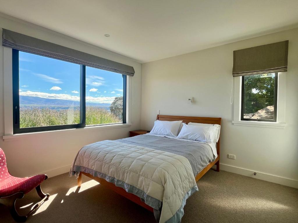 a bedroom with a bed and two large windows at Mountain and river view retreat in Alexandra