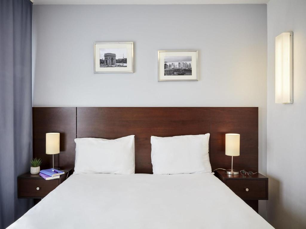 Un dormitorio con una gran cama blanca con dos lámparas. en Aparthotel Adagio Access Paris Bastille, en París