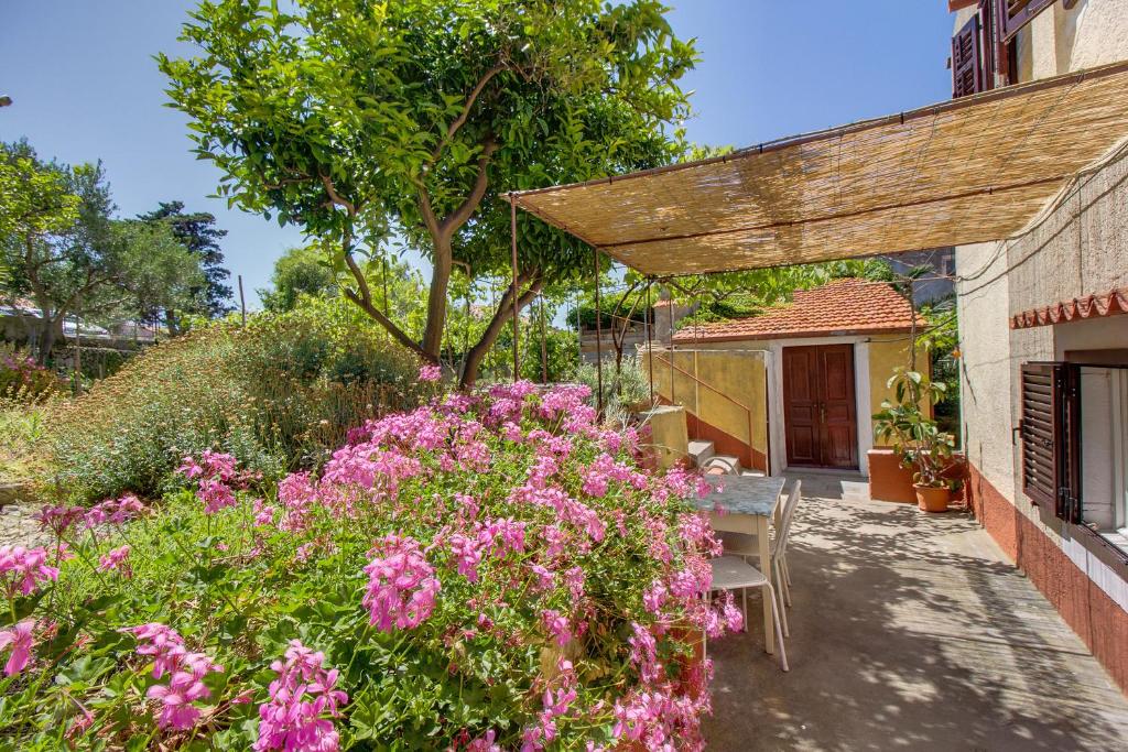 un jardín con flores rosas y pérgola de madera en Holiday Home Lina Cipollina en Mali Lošinj