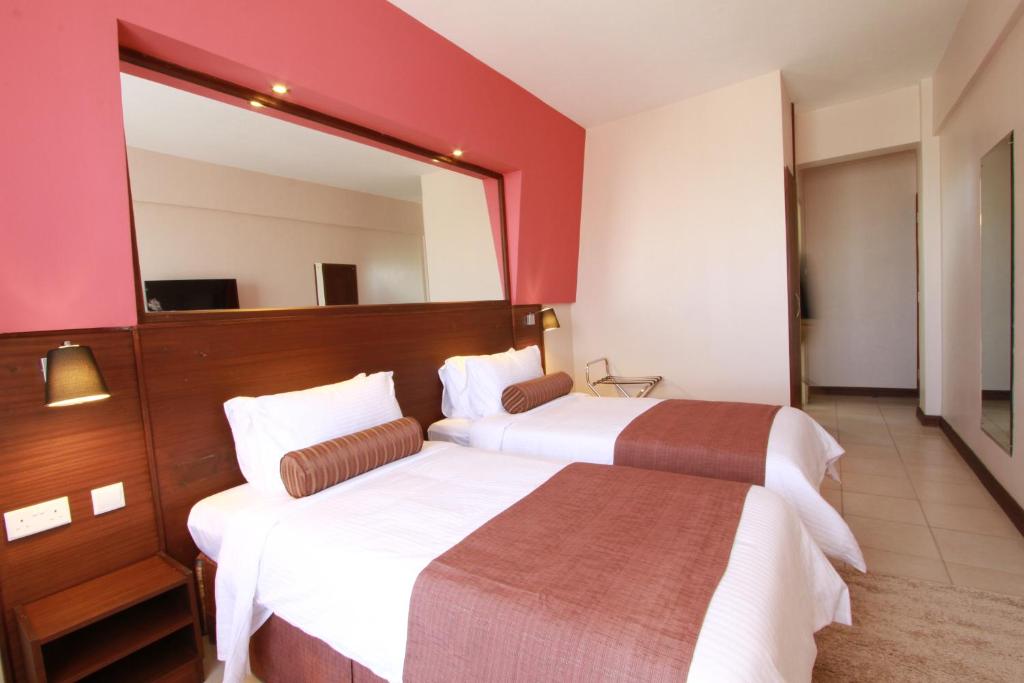 two beds in a hotel room with a mirror at Hotel Rio in Nairobi