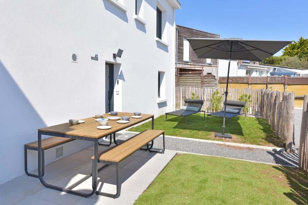 a patio with a wooden table and benches and an umbrella at Piriac Norven Appartement maison 6p 500m plage in Piriac-sur-Mer