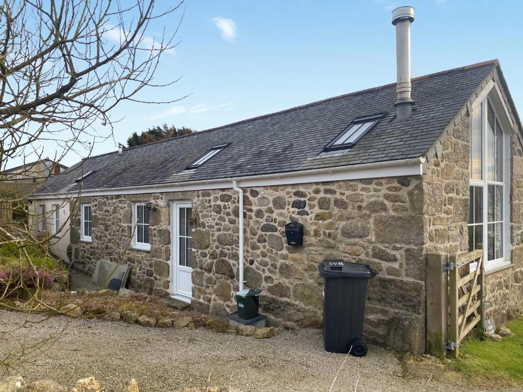 una casa de campo de piedra con un cubo de basura delante de ella en The Milking Parlour, en St Ives