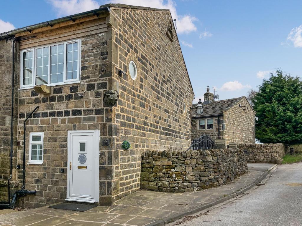 a brick building with a white door and a stone wall at Bank Top Mews - Uk49214 in Wilsden