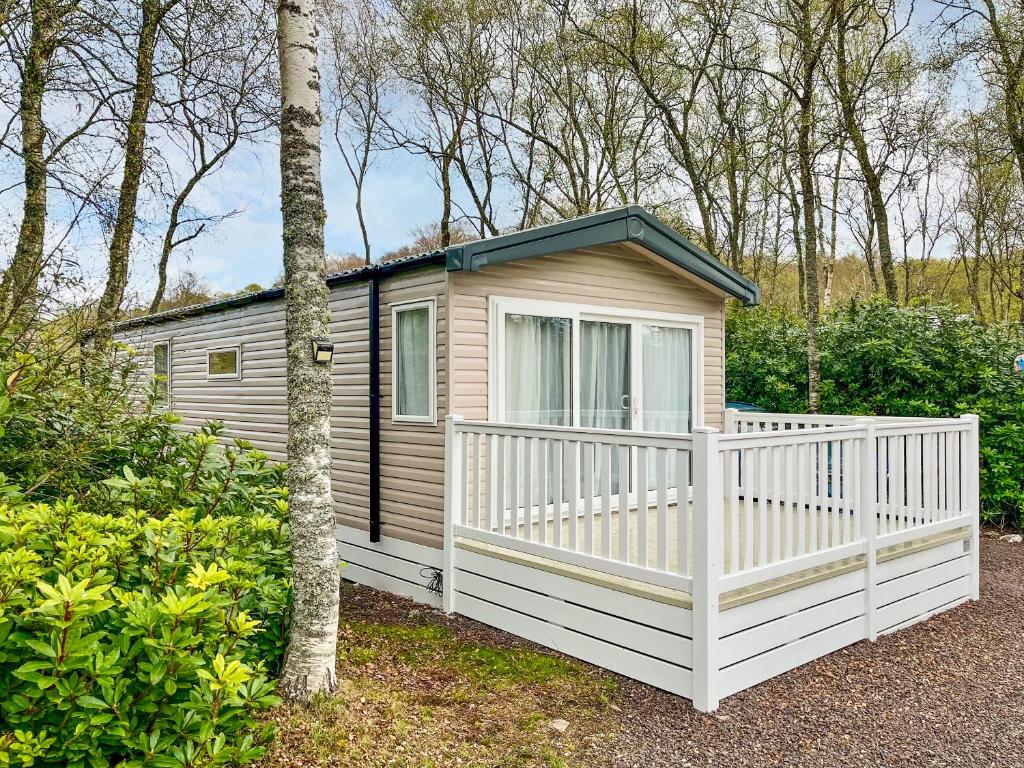 a small cabin with a white fence in a yard at Woodland Serenity in Edzell