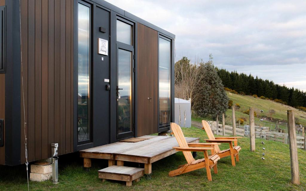 a house with a wooden bench and two chairs at Bruce Farm Alpaca Cabin 1 by Tiny Away in Balclutha