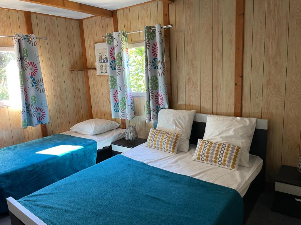 2 Betten in einem Zimmer mit Holzwänden und Fenstern in der Unterkunft Camping La Montagne in Sorgues