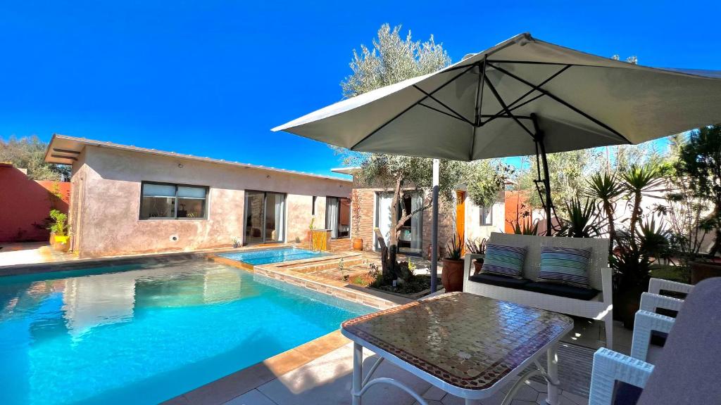 ein Tisch mit Sonnenschirm neben einem Swimmingpool in der Unterkunft Villa Romantique à Marrakech Avec Piscine Privée & Jardin in Marrakesch
