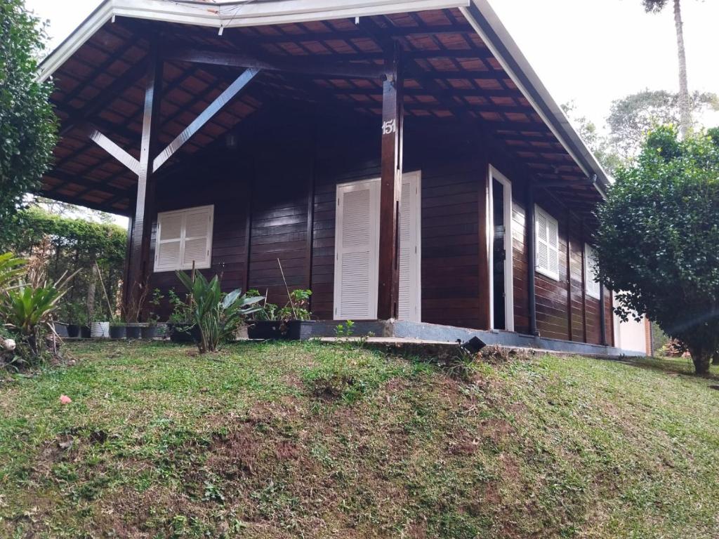 a wooden house with a porch and a grass yard at Casa campos recanto in Campos do Jordão