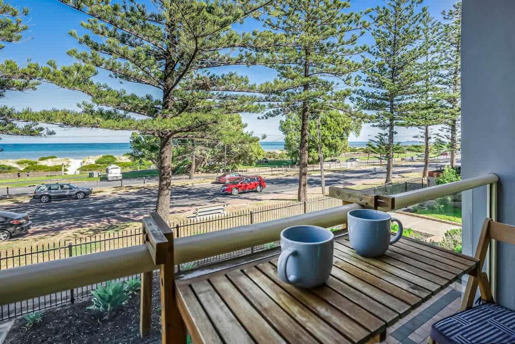 a wooden bench on a balcony with two mugs on it at Beachfront self contained upstairs apartment in Semaphore