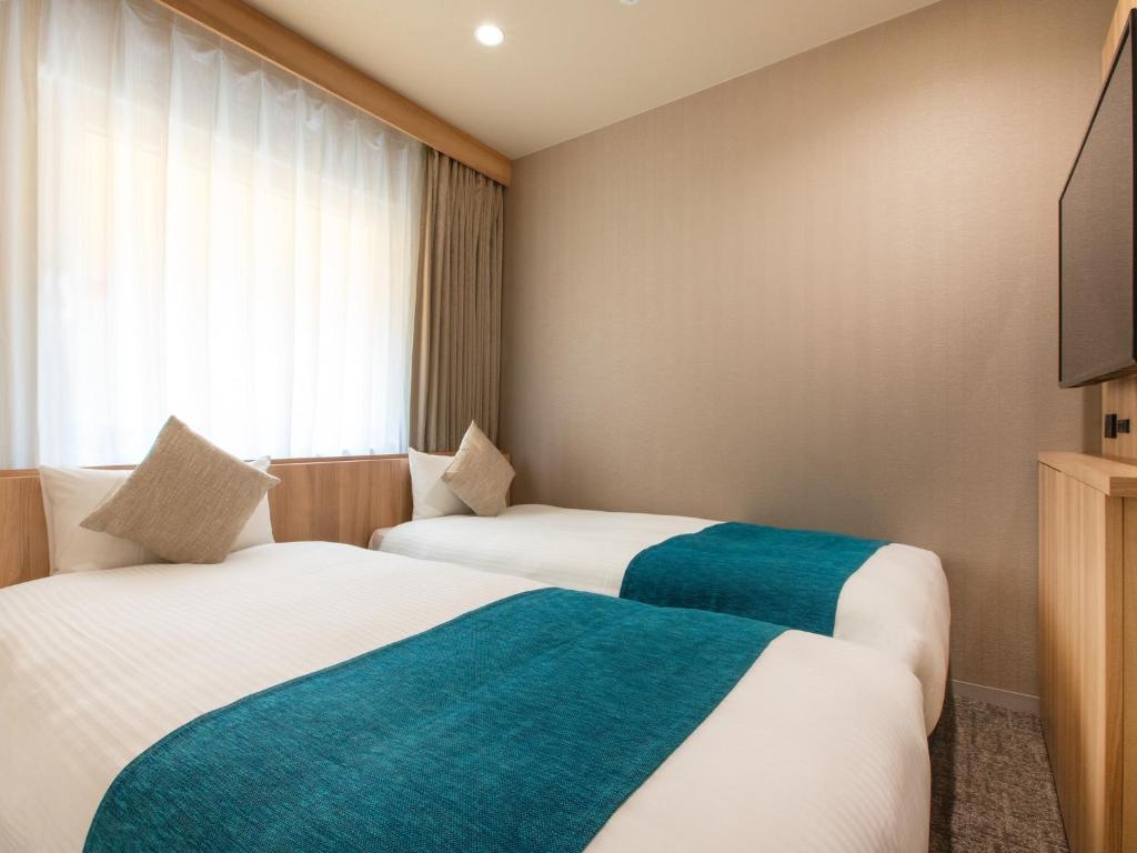 two beds in a hotel room with a window at Villa Fontaine Tokyo Jimbocho in Tokyo