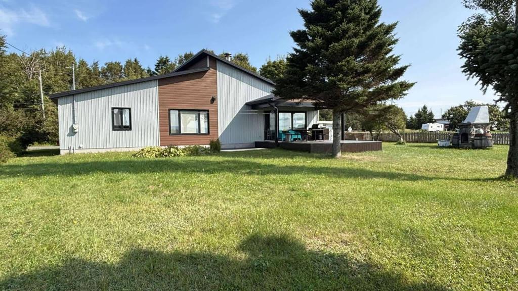 a small white house with a tree in a yard at Spa & Nature - LAncrage in Rivière-Ouelle