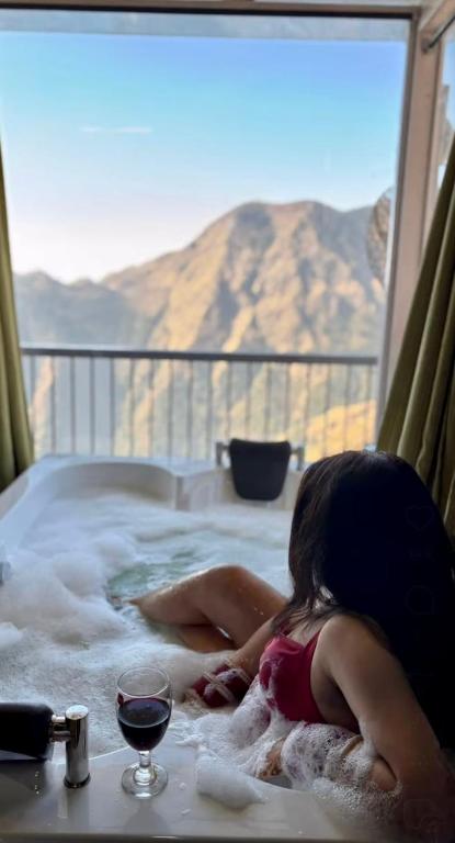 a woman laying in a hot tub with a glass of wine at Panoramic Jacuzzi Suite with huge Balcony & Swing in Mussoorie