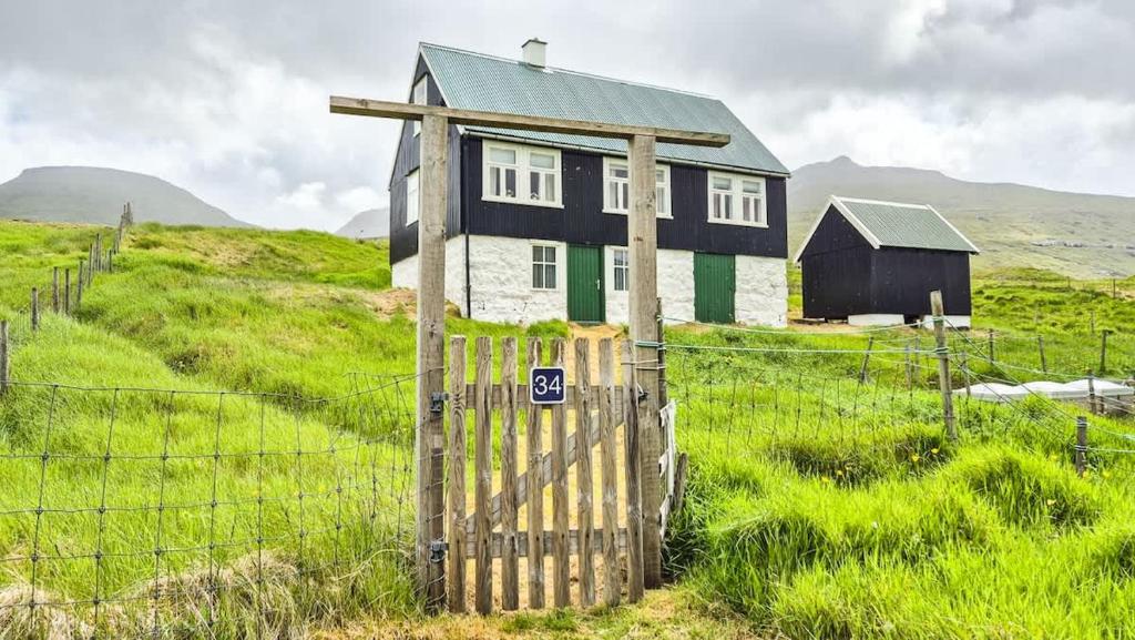 une maison noire et blanche dans un champ avec une clôture dans l'établissement Unique & Charming Faroese Cottage, à Norðskáli