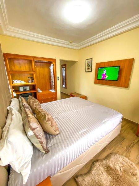 a bedroom with a bed with a tv on the wall at Hotel Vallée Des Princes in Douala