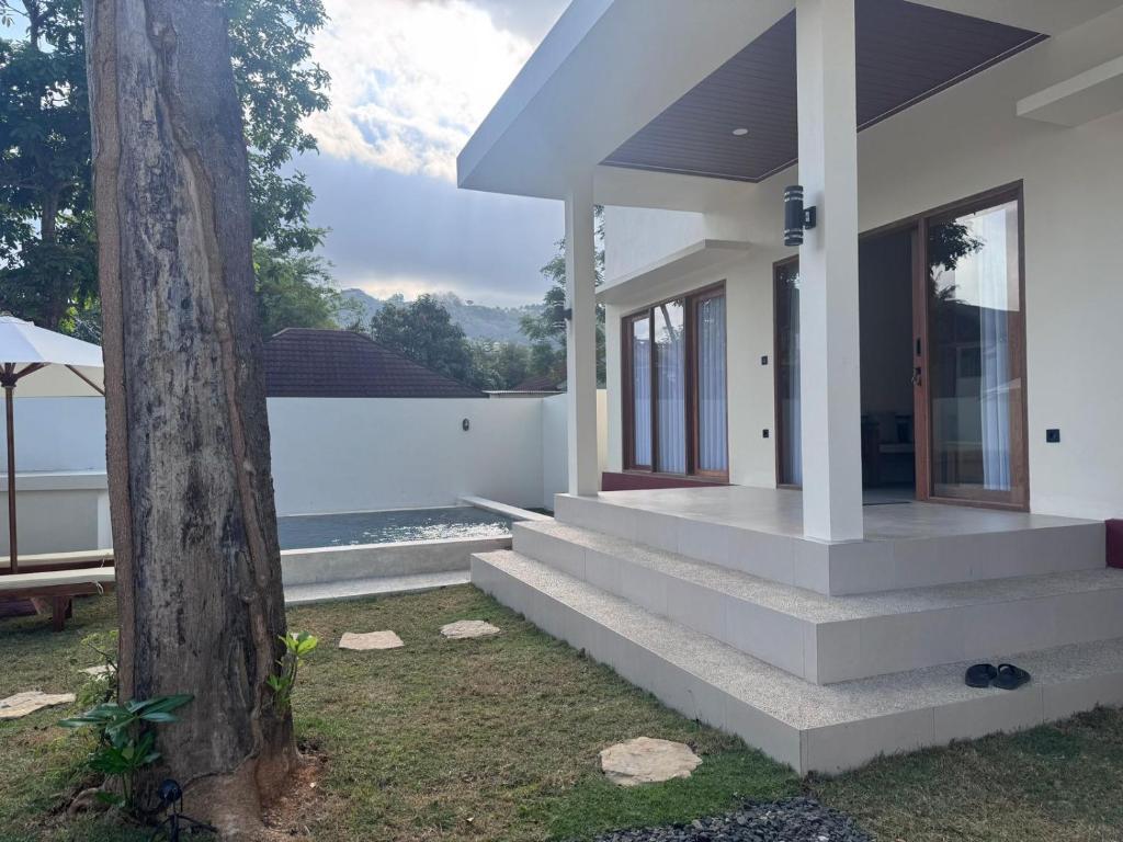 a white house with stairs next to a tree at Permata Villas Lombok in Kuta Lombok