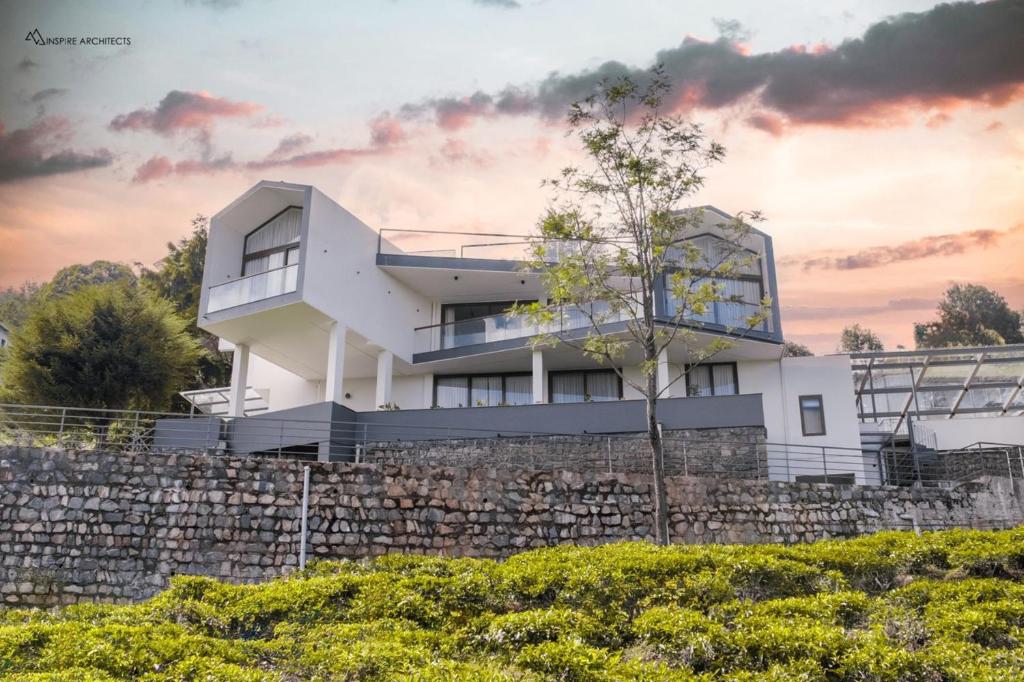 a white house behind a stone wall at Hills and Heart Luxury Villa By LexStays in Coonoor