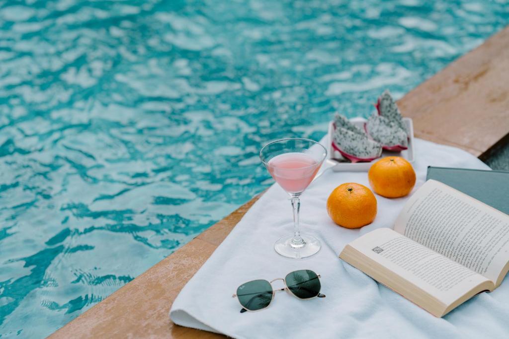 A styled poolside tray with a drink, fruit, sunglasses, and an open book.
