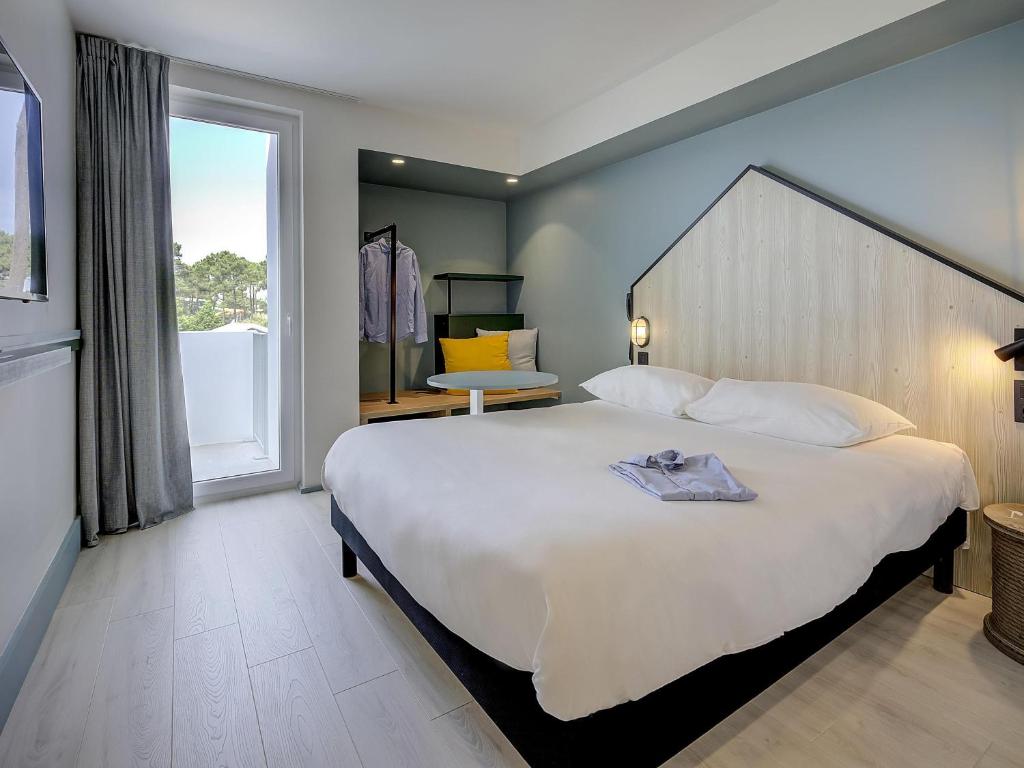une chambre avec un grand lit et une grande fenêtre dans l'établissement ibis Styles Arcachon Gujan Mestras, à Gujan-Mestras