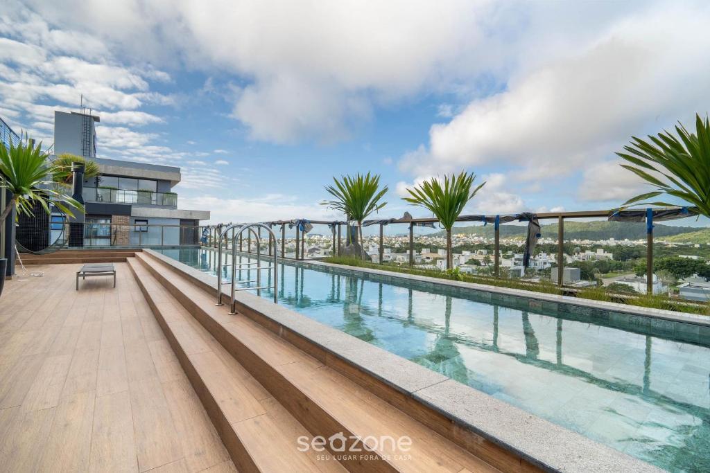a swimming pool on the roof of a building with palm trees at Apto c/ varanda e churrasqueira em Jurerê IHD0101 in Florianópolis