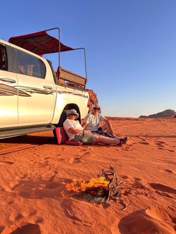 a family sitting next to a truck in the desert at Desert Life Camp Wadi Rum in Wadi Rum