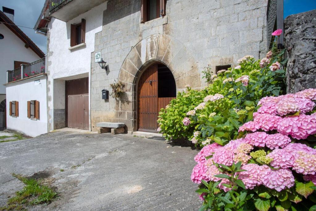 un edificio con una porta di legno e alcuni fiori rosa di Casa rural Txorrota Txortako Txikia Selva de Irati a Orbaizeta