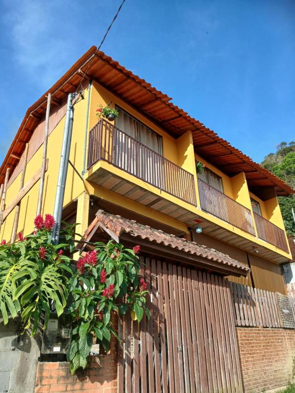 una casa amarilla con balcón y flores. en Kasadidani Suítes em Lumiar, en Nova Friburgo
