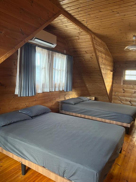two beds in a wooden room with two windows at ISE Family Cabin in Ise