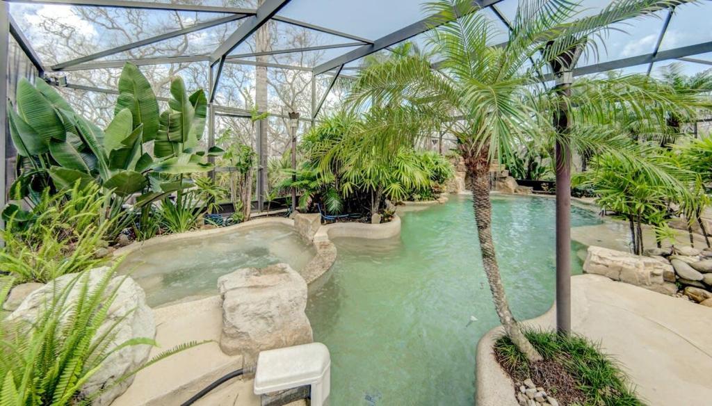 Una piscina en un invernadero con una palmera. en Beach Home with Amazing Oasis Pool Spa Waterfall Fire Pit Bikes, en Marineland