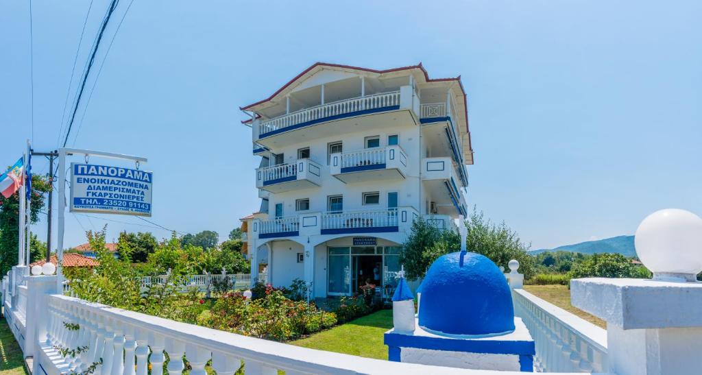 a white building with blue balconies on a white fence at Panorama Apartments in Paralía Skotínis