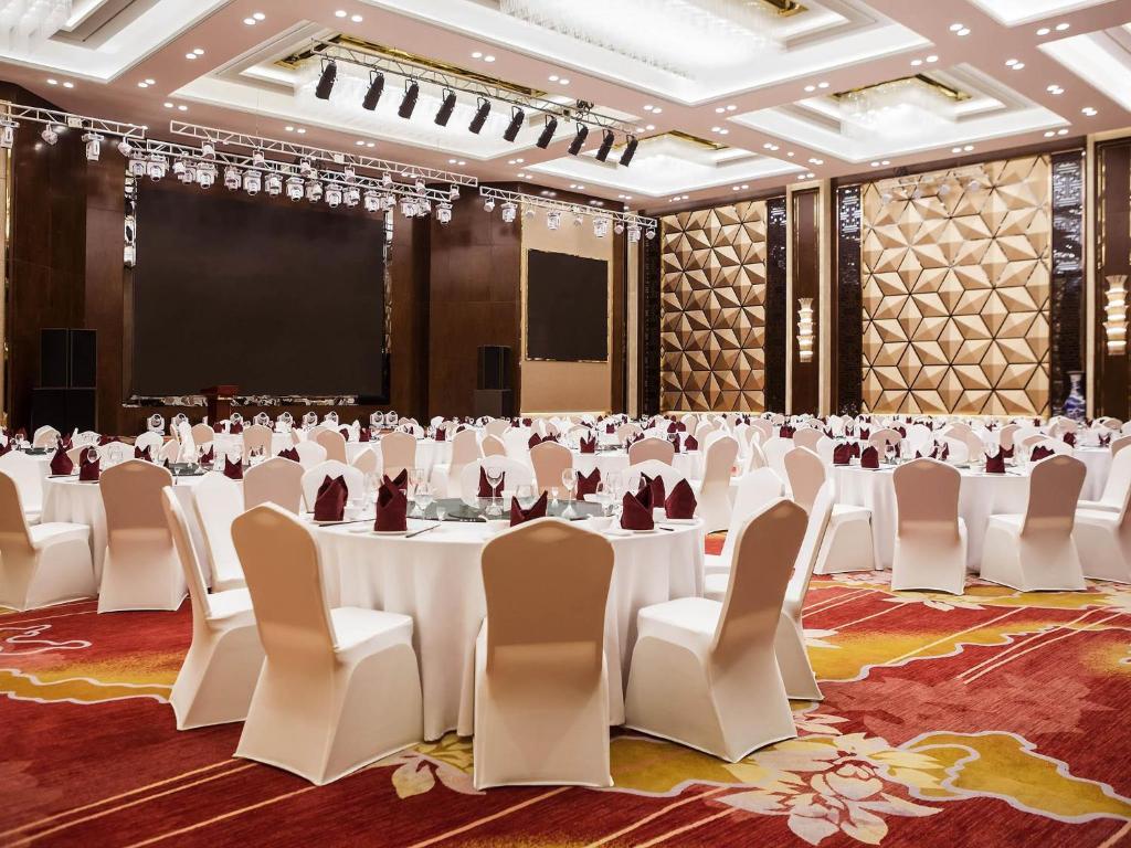 a banquet hall with white tables and chairs and a screen at Novotel Daqing Haofang in Daqing