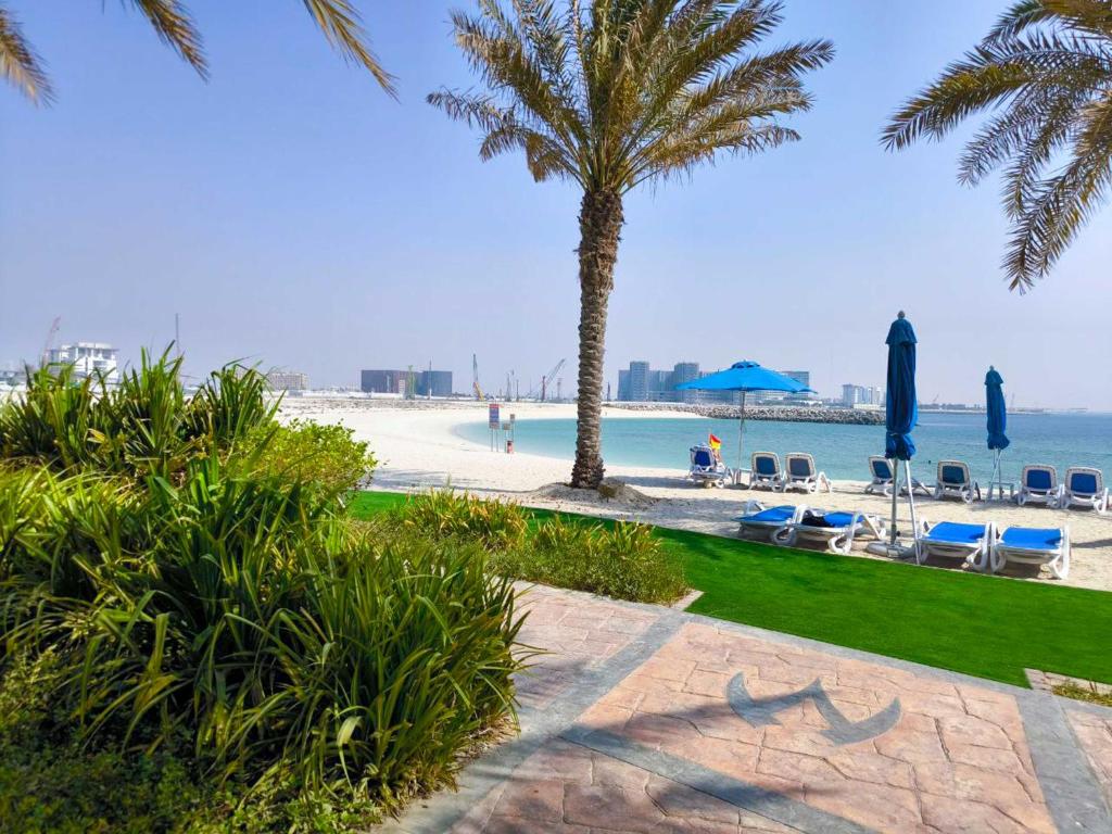 a beach with palm trees and chairs and the ocean at Modern 1BR with Beach and Pool in Al Marjan Island in Ras al Khaimah
