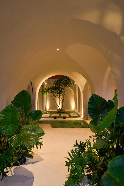 A softly lit arched passage leads through dense tropical planting to a central tree.