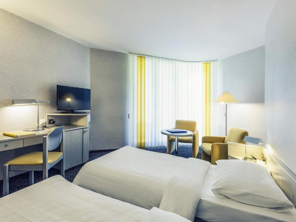 a hotel room with two beds and a desk at Mercure Lenzburg Krone in Lenzburg