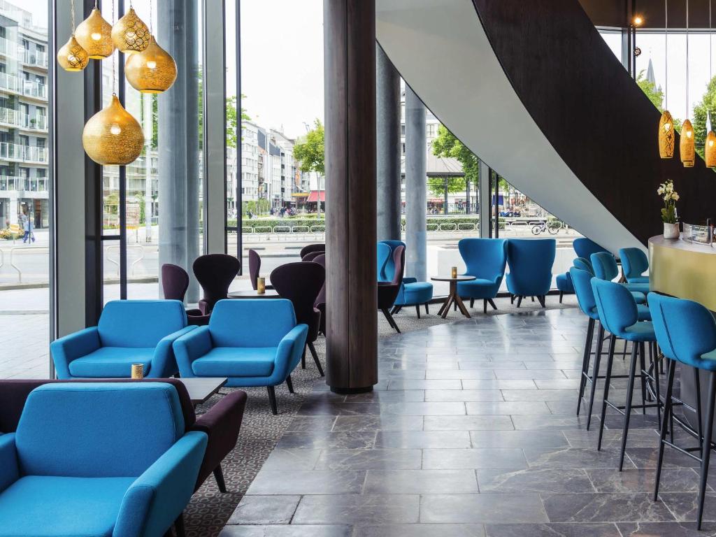 a lobby with blue chairs and tables and windows at Mercure Blankenberge in Blankenberge