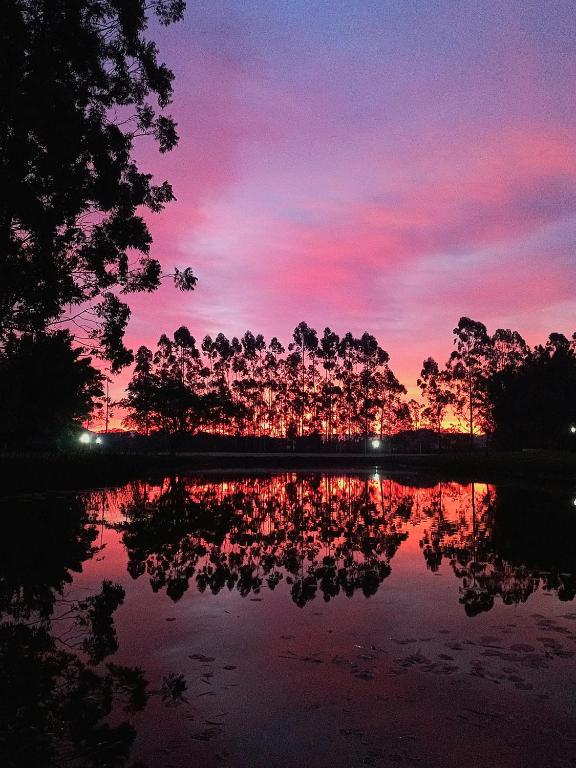 a sunset with a reflection of trees in a lake at Propriedade inteira - duas suítes, pavilhão e espaço externo in Passo De Torres