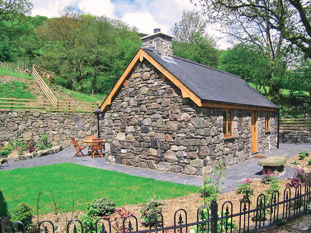 Un edificio de piedra en un jardín con una valla. en Yr Efail - Hw7387, en Llanymawddwy