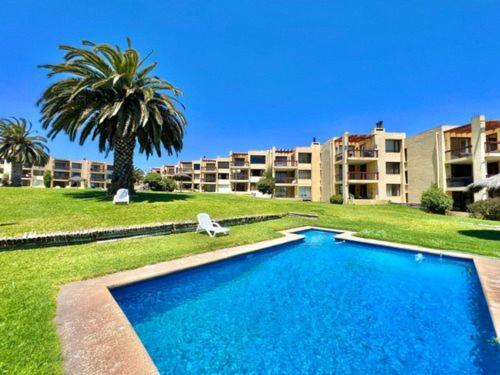 MAITENCILLO VISTA BOSQUE y MAR في مايتنسيلو: حمام سباحة أمام مبنى به شجرة نخيل