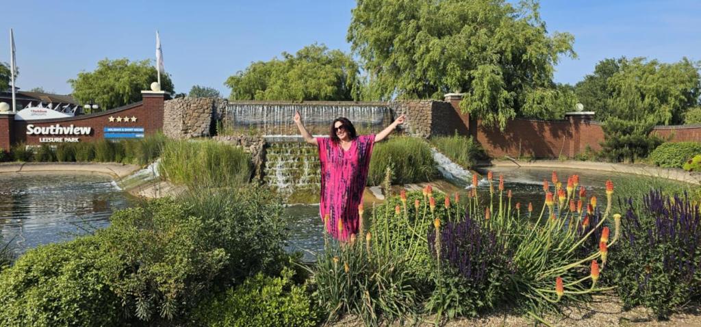 Una mujer con un vestido rosa parada frente a un estanque. en Serenity Nook, en Skegness