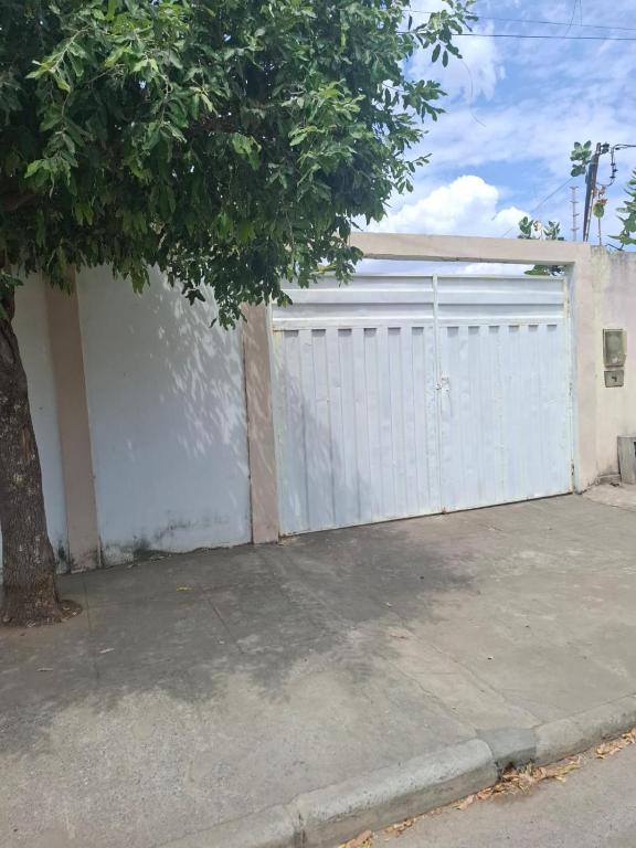 a white garage door with a tree next to a sidewalk at CasaBomJesusdaLapa 2 quartos in Bom Jesus da Lapa