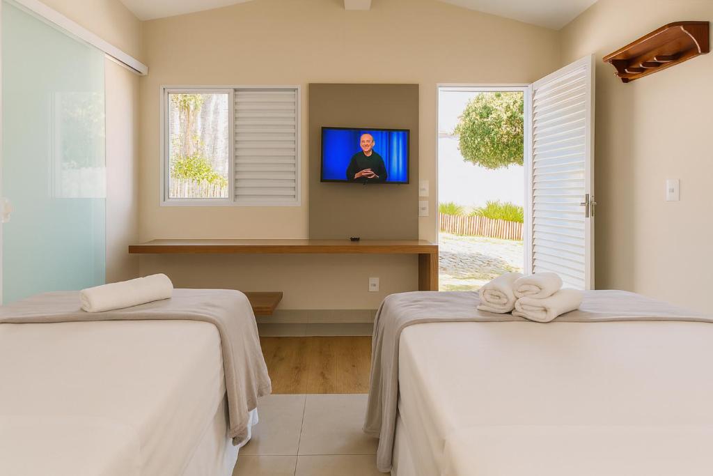 deux lits dans une chambre avec une télévision au mur dans l'établissement Vila da Praça Pousada, à Capitólio