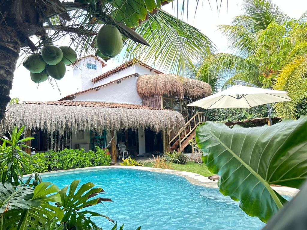 a swimming pool in front of a house with an umbrella at Pousada Tatuamar Café & Bistrô - 150 m da praia in Pôrto de Pedras