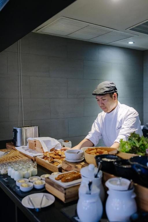 A chef works behind a breakfast buffet lined with pastries, bowls and condiments.