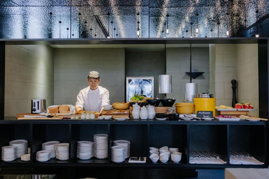 A chef stands behind a fully set breakfast buffet with plates, bowls and serving dishes.