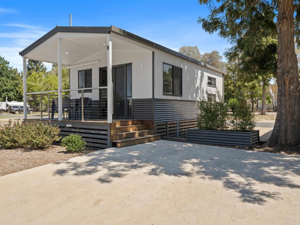 a small white house with a porch and a tree at Wodonga Holiday Park in Wodonga